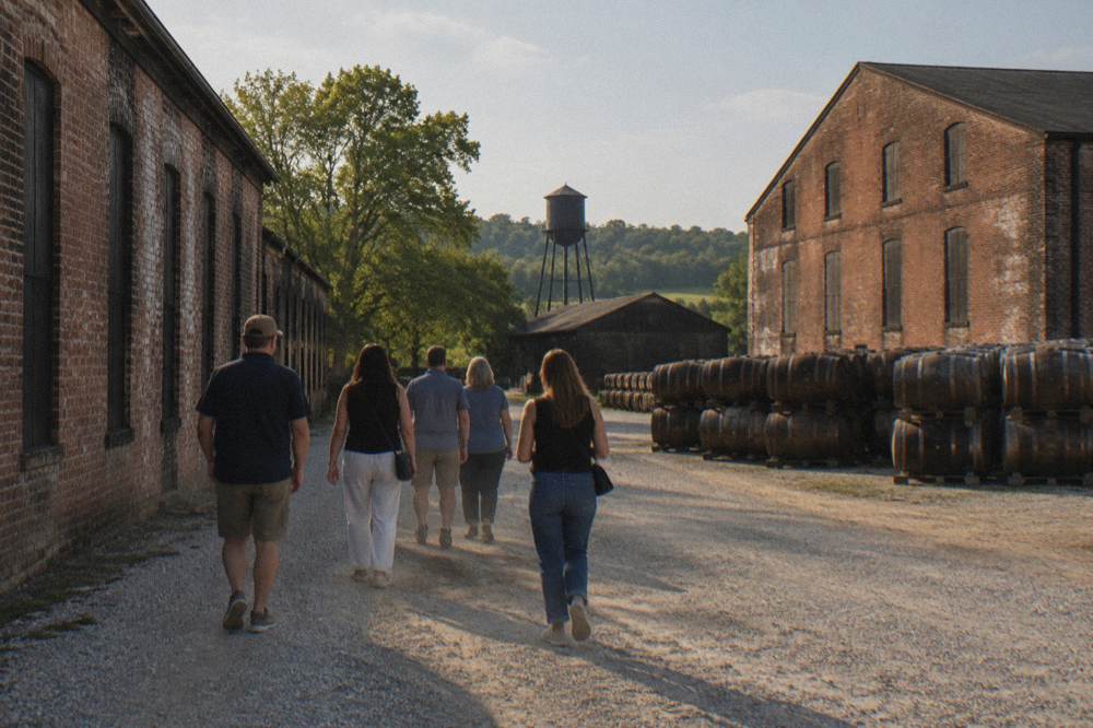 A guided bourbon tour group walking between brick warehouses on a Kentucky distillery campus