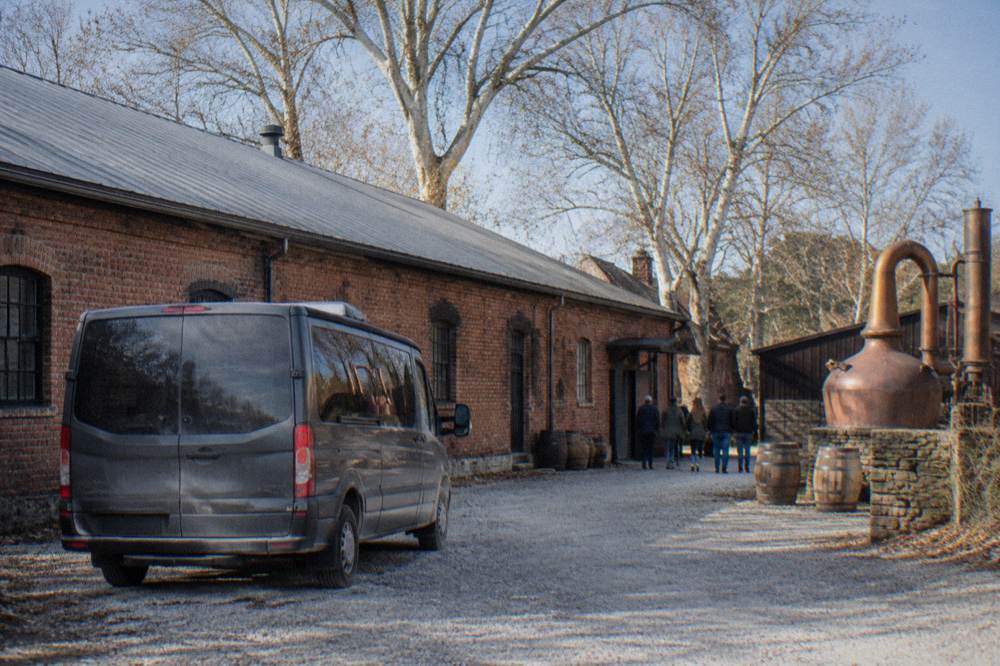 Guided tour van parked on a rural road beside a Kentucky distillery building